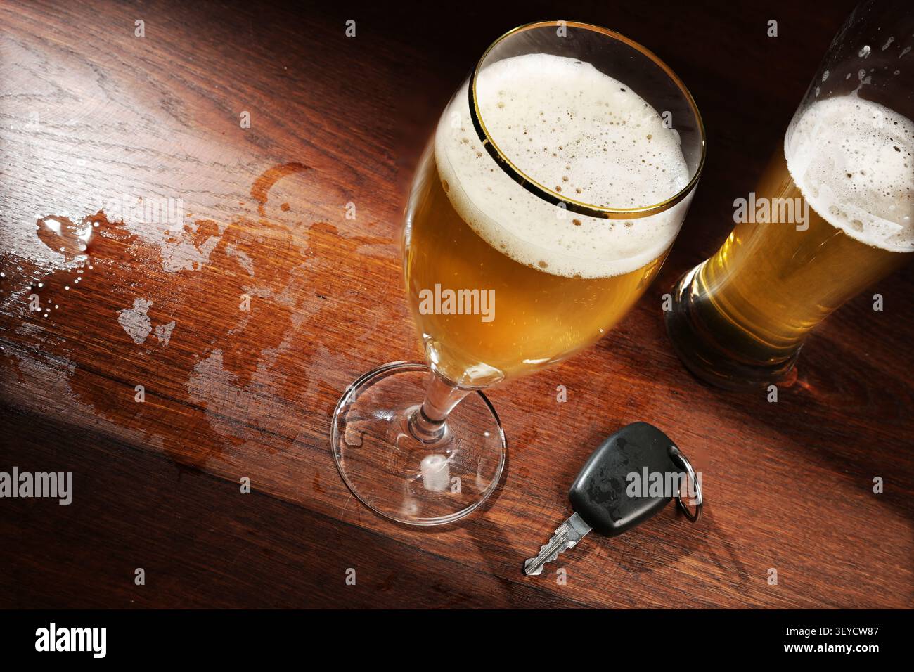 Zwei Biergläser und ein Autoschlüssel an der dunklen Holzbar in einem Pub, Konzept gegen gefährliches Fahren nach Alkoholkonsum, Kopierraum, ausgewählter Fokus Stockfoto