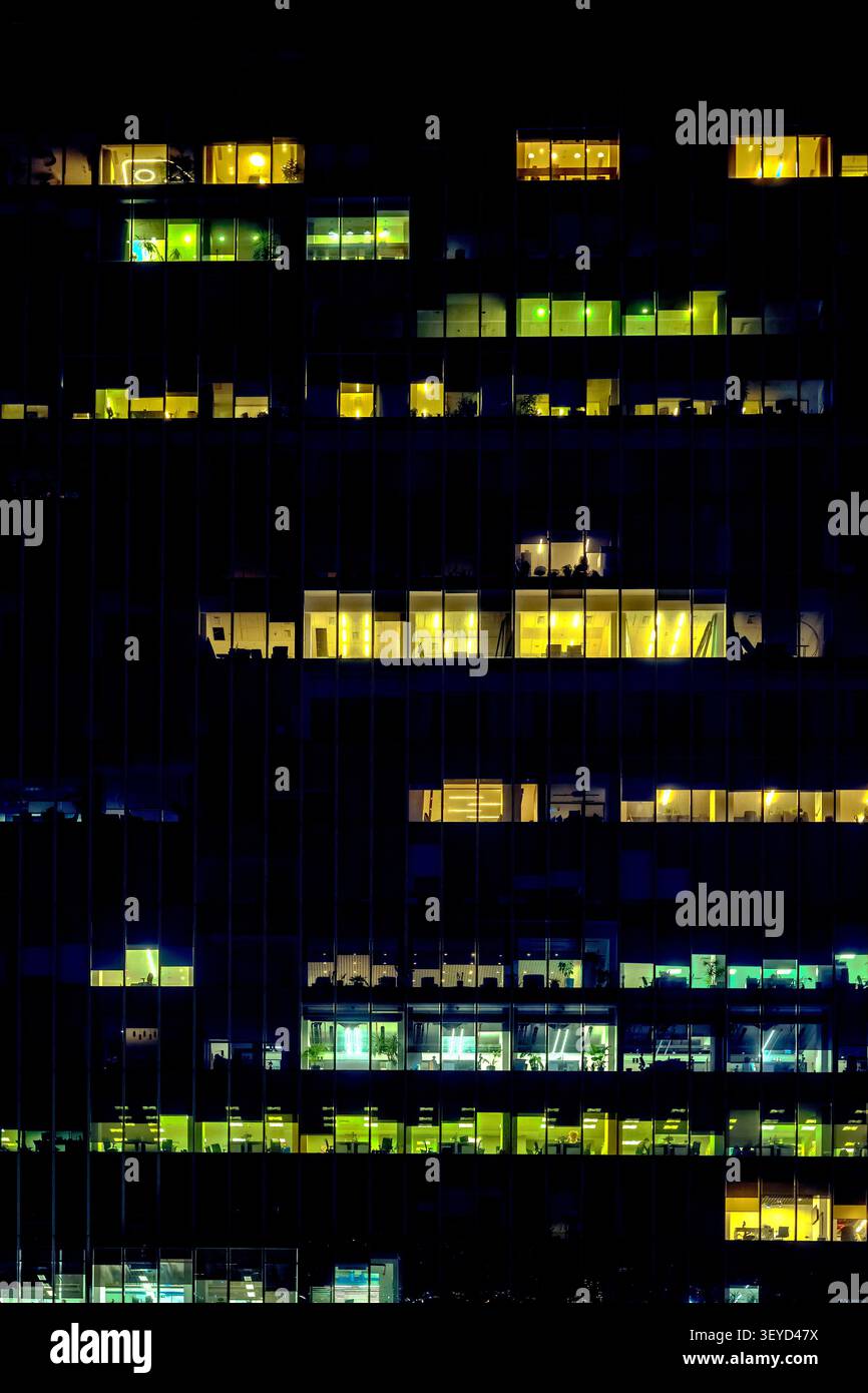Beleuchtete Bürofenster an einer dunklen Glasfassade in der Nacht, die ein abstraktes Muster aus Licht und Schatten schaffen. Stockfoto