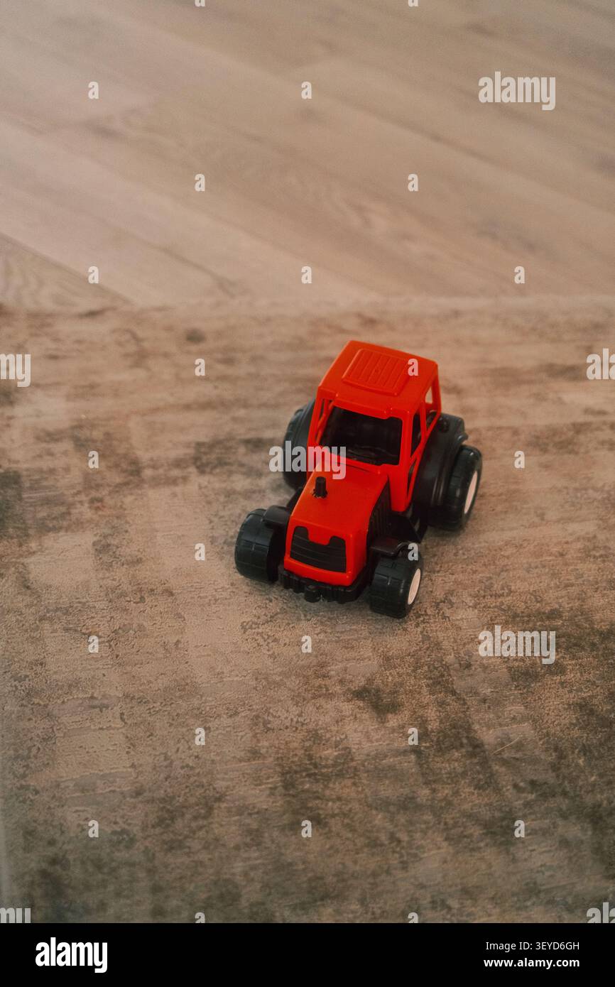 Roter Miniatur-Spielzeugtraktor auf sauberem Holzboden mit Kopierraum. Geeignet für die Erziehung von Kindern, landwirtschaftliche Konzepte und fantasievolle Spiele. Stockfoto