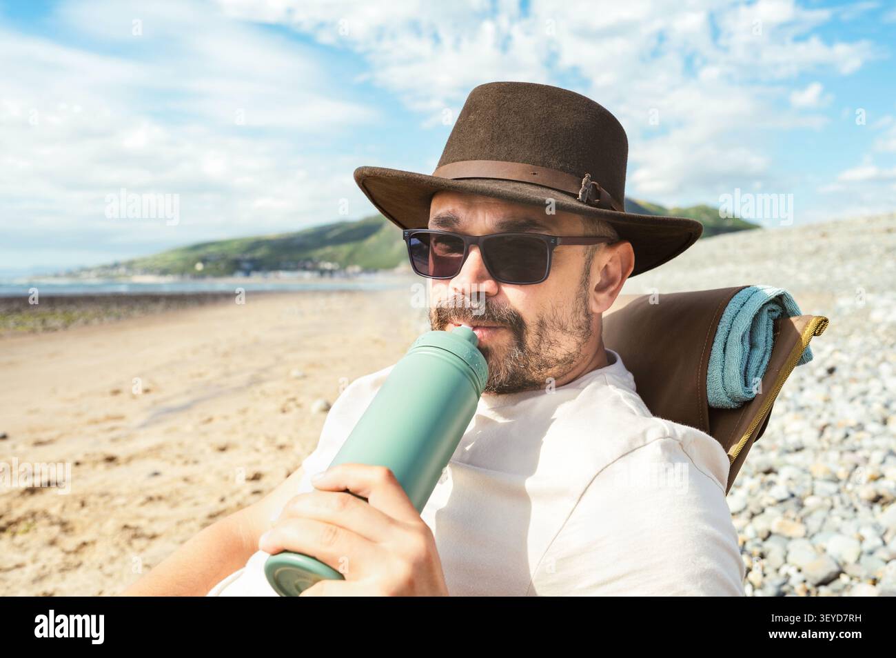 Mann trinkt aus einer wiederverwendbaren Flasche, während er sich draußen entspannt Stockfoto