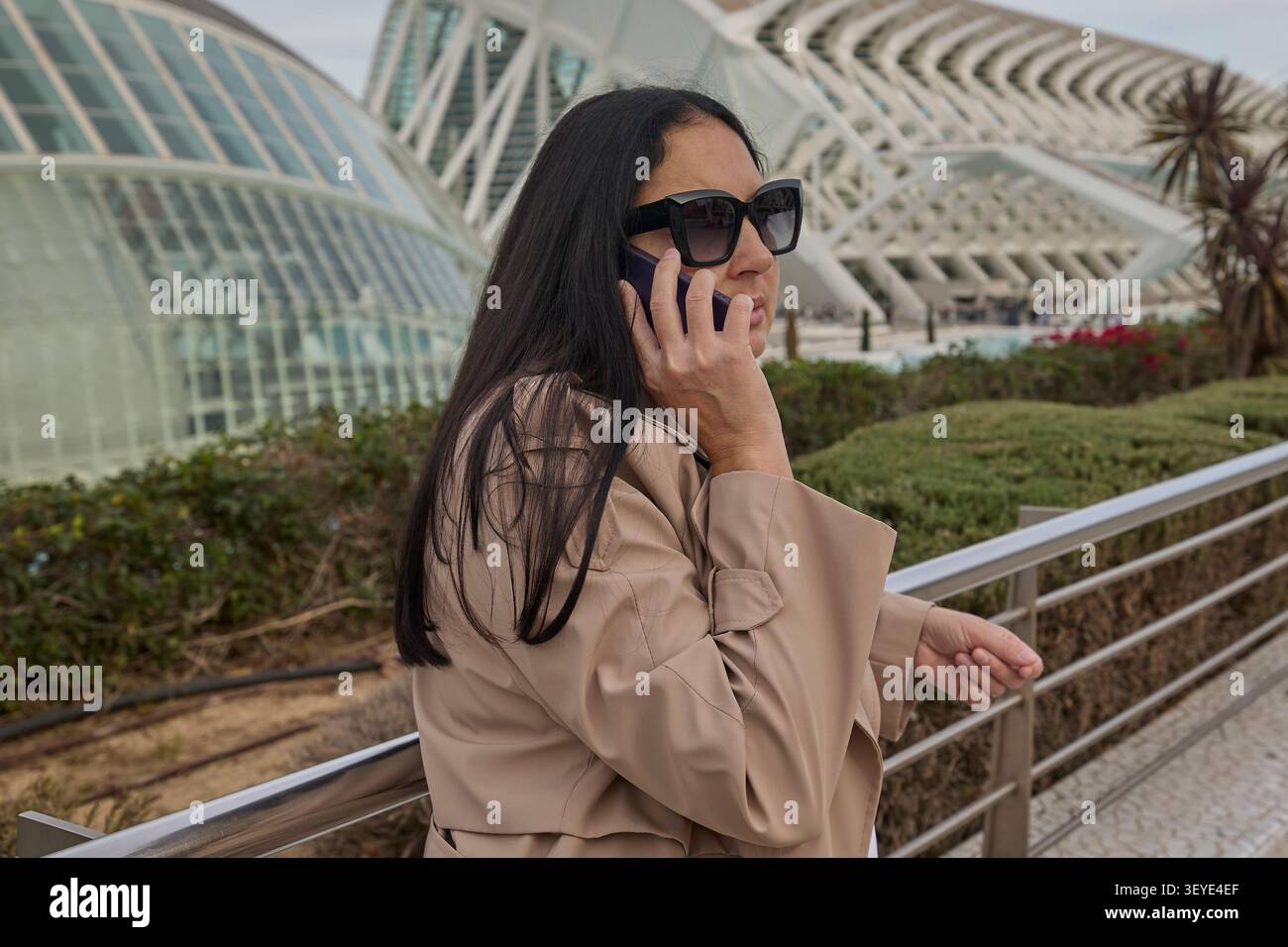 Frau in Sonnenbrille, die auf dem Smartphone in der Nähe eines futuristischen Gebäudes spricht. Kommunikation und urbanes Lifestyle. Stockfoto