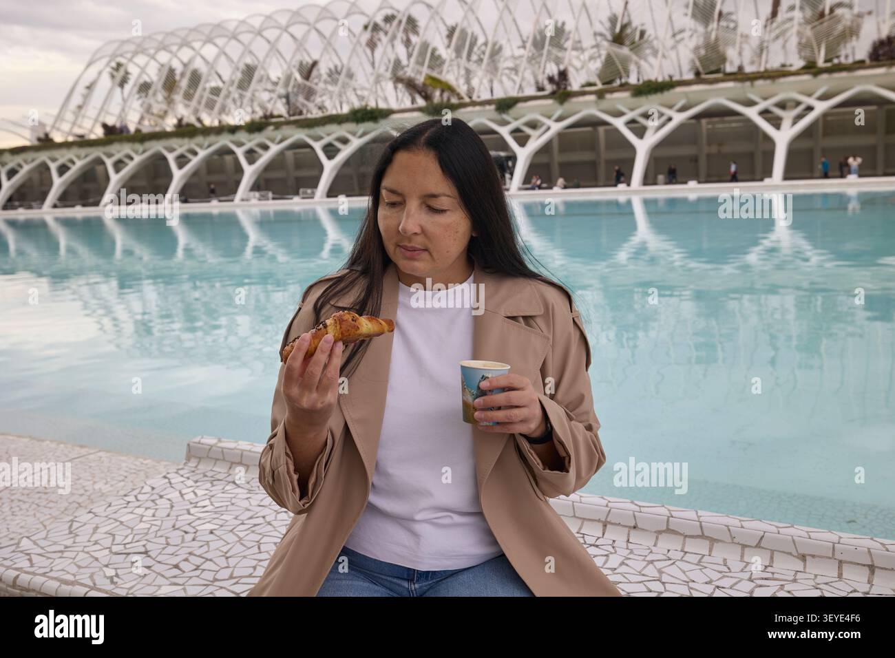 Frau hält Kaffee und Gebäck in der Nähe des Wassers. Entspannter Lifestyle-Moment. Stockfoto