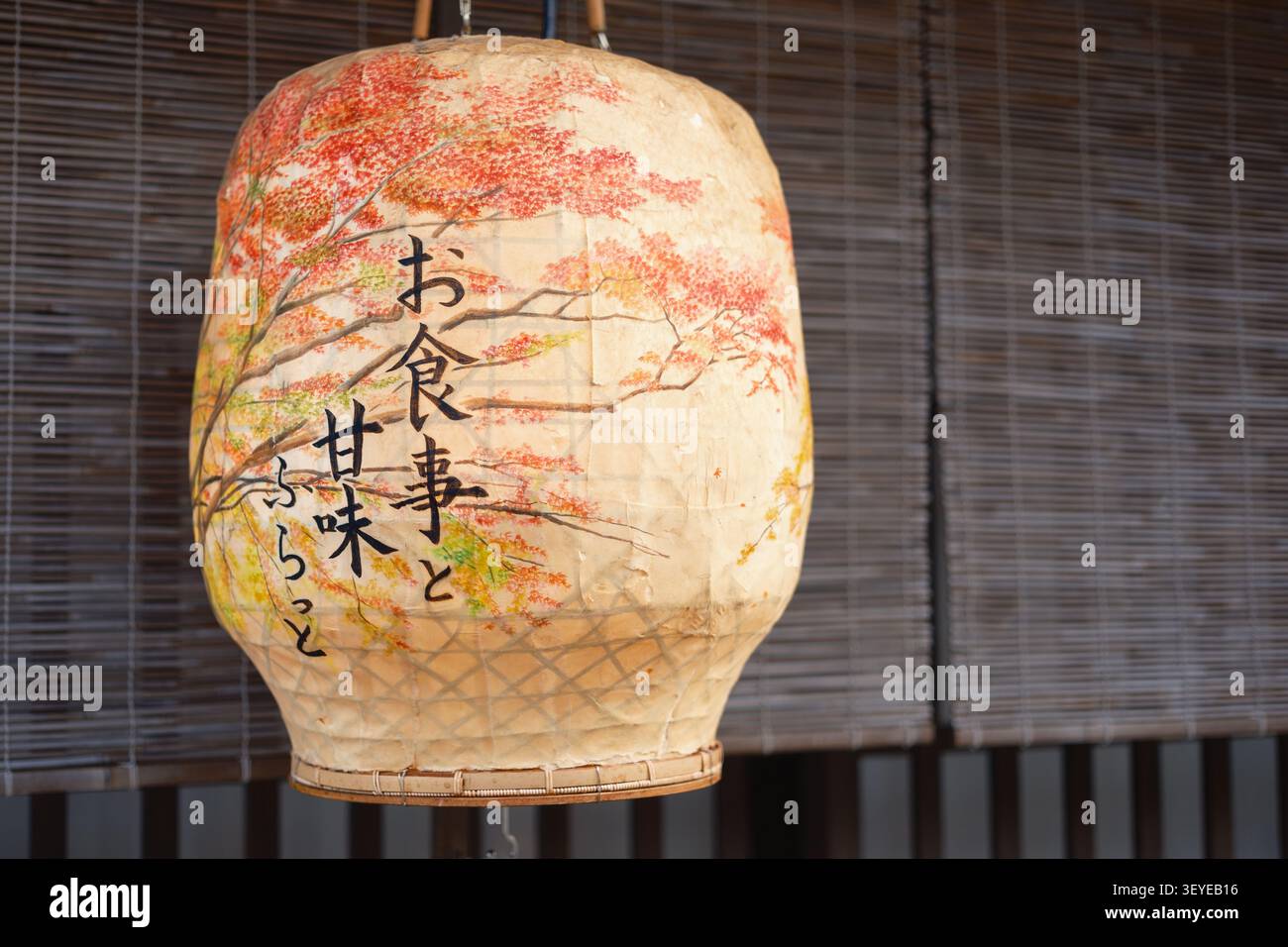 Eine traditionelle handbemalte japanische Papierlaterne mit gemalten Kanji-Zeichen, die nachts vor einem dunklen, mit Holzlatten verkleideten Fenster in Kyoto, Japan, hängt Stockfoto