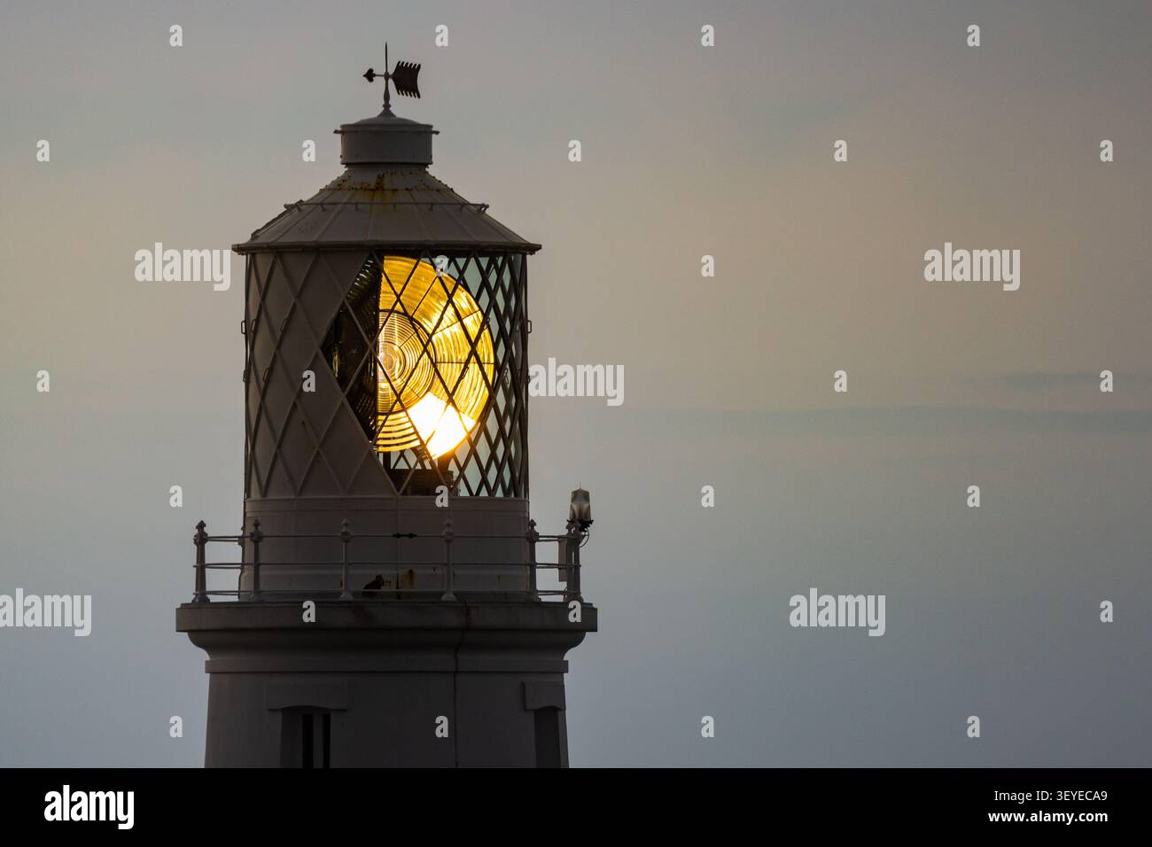 Eine Nahaufnahme, die sich auf den beleuchteten Glaskuppelsaal und den Optiklinsemechanismus des Strumble Head Leuchtturms bei Dämmerung in Pembrokeshire konzentriert Stockfoto