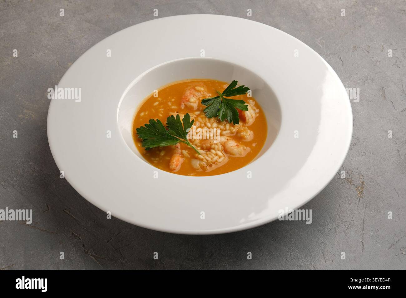 Reissuppe mit Meeresfrüchten, Garnelen und Petersilie, serviert in einer breiten weißen Schüssel auf grauer Steinoberfläche Stockfoto