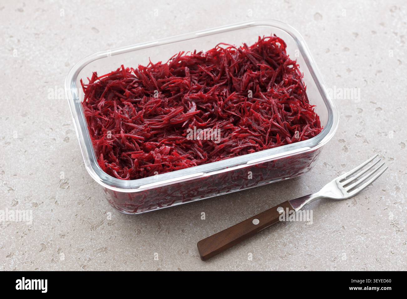 Frischer geriebener Rote-Bete-Salat in einem Glasbehälter mit Gabel auf einer hellen Steinoberfläche. Gesundes Gemüsegericht, Mahlzeit Zubereitung Zutat Stockfoto