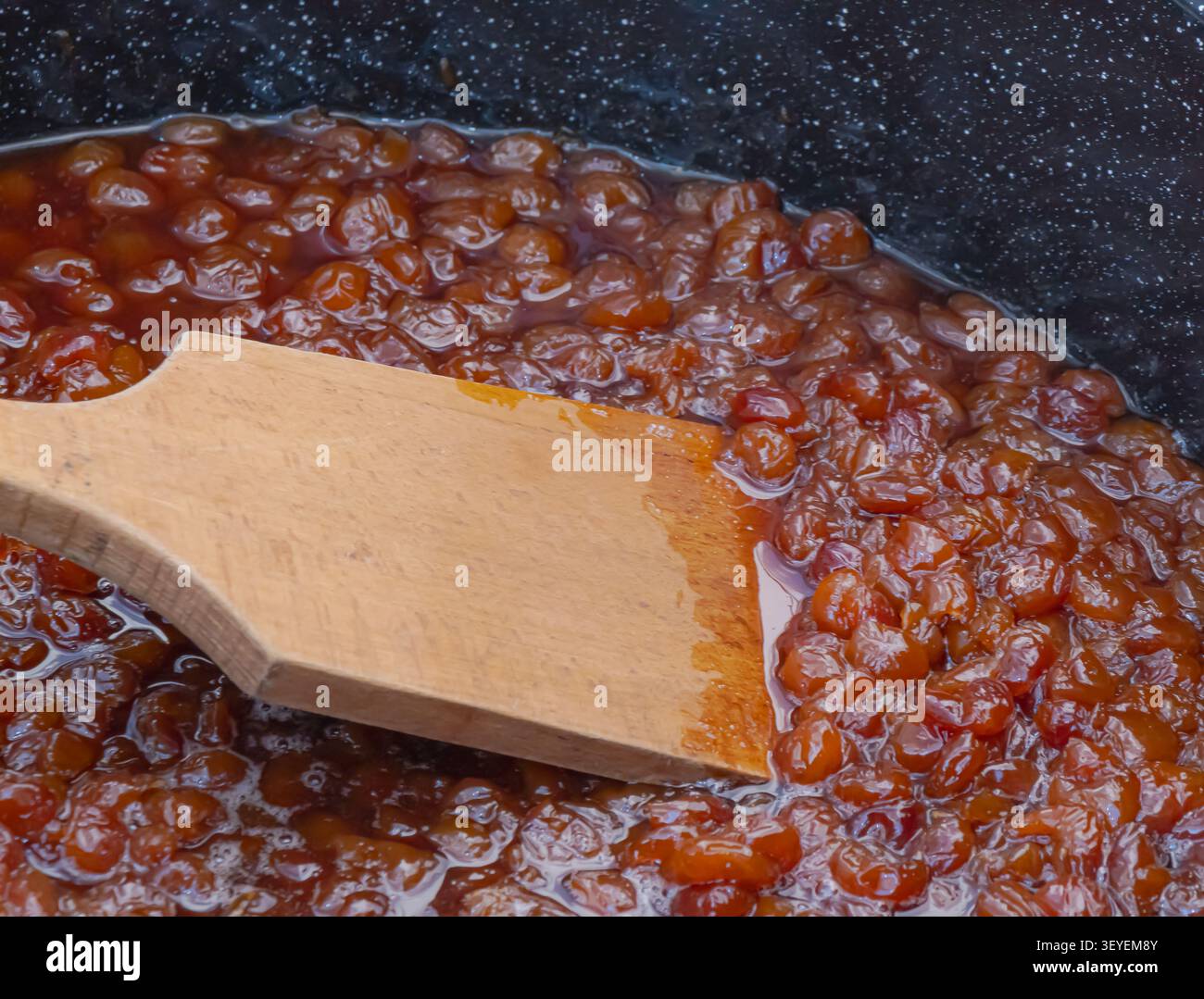 Hausgemachte gelbe Kirschmarmelade, die in einem Kochtopf mit Holzspachtel während der traditionellen Zubereitung von Obstkonserven und der saisonalen Konservierung kocht. Stockfoto