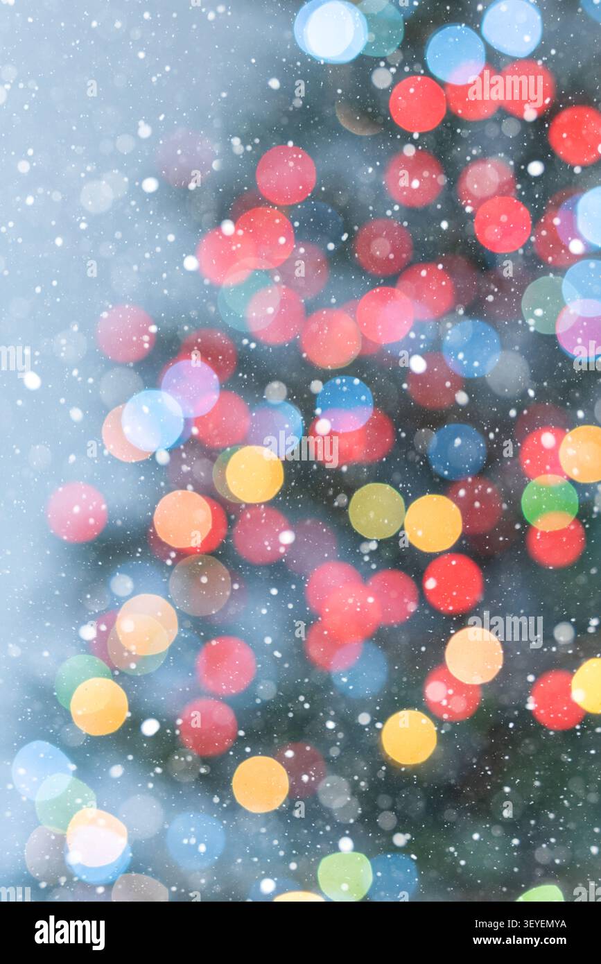 Vertikaler Feiertagshintergrund mit bunten Weihnachtsbaum-Bokeh-Lichtern auf einem weichen hellblauen Hintergrund. Fallender Schnee und die subtile Kontur von Stockfoto
