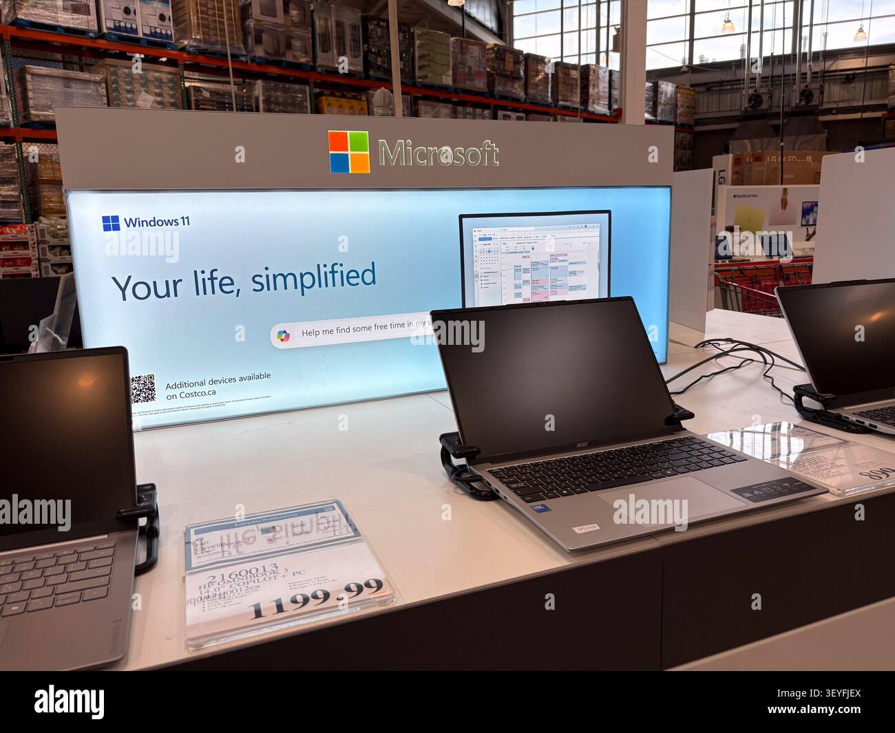 Laptops in einem Einzelhandelsgeschäft mit Microsoft Windows 11-Schildern und Produktinformationen zu Werbeaktionen. Stockfoto