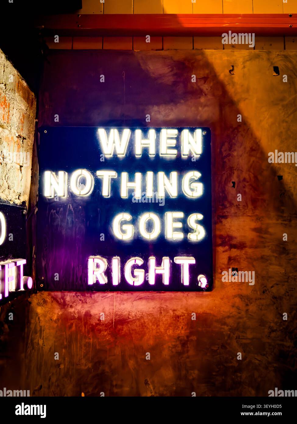 Beleuchtetes Neonschild an einer strukturierten Wand & Betonhintergrund mit dem Text WHEN NOTHING GOES RIGHT, malaysia - Smartphone-aufgenommenes Stockfoto