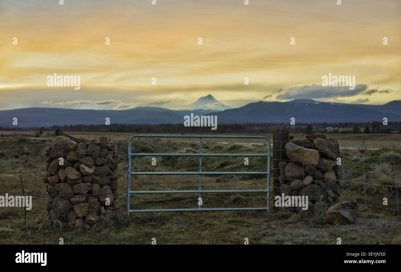 Rustikales Farm Gate und Steinsäulen öffnen sich zu einem majestätischen Sonnenuntergang am Berg Stockfoto