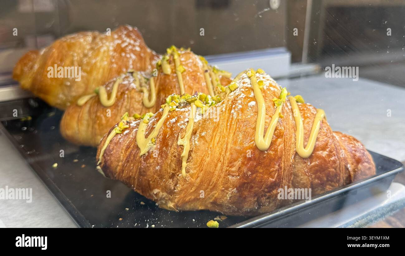 Goldene Croissants mit Pistaziennebel auf einem Tablett in einer Bäckerei. Der knusprige Teig mit nussigem Topping sorgt für ein appetitliches Erscheinungsbild Stockfoto