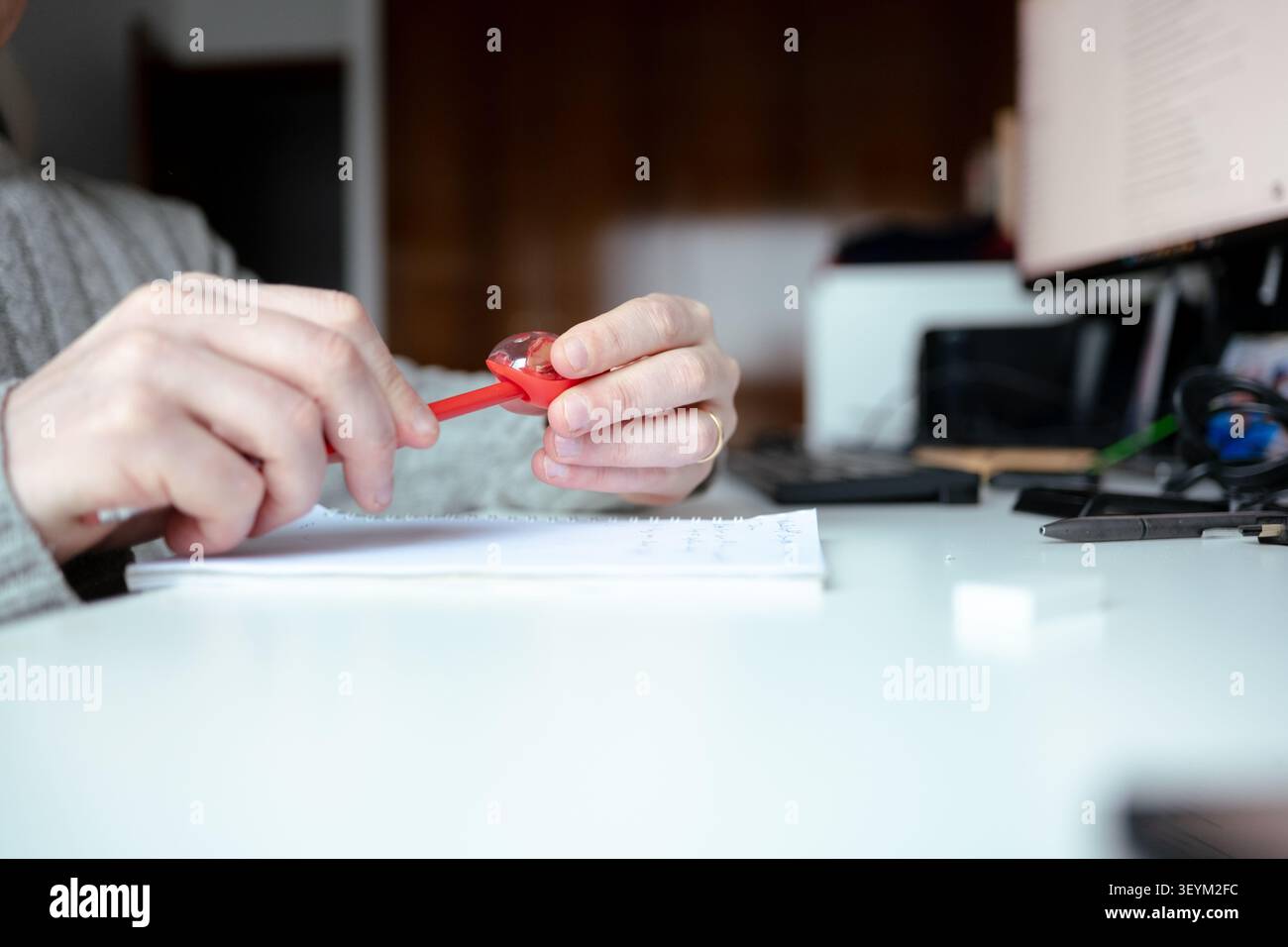 Hände, die einen roten Bleistift über offenem Notizbuch auf einem weißen Schreibtisch schärfen Stockfoto
