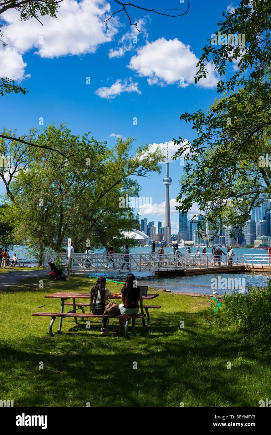 Toronto, Ontario, Kanada - 20. Juni 2026: Zwei Frauen sitzen an einem Picknicktisch und essen mit der Skyline von Toronto im Hintergrund zu Mittag Stockfoto