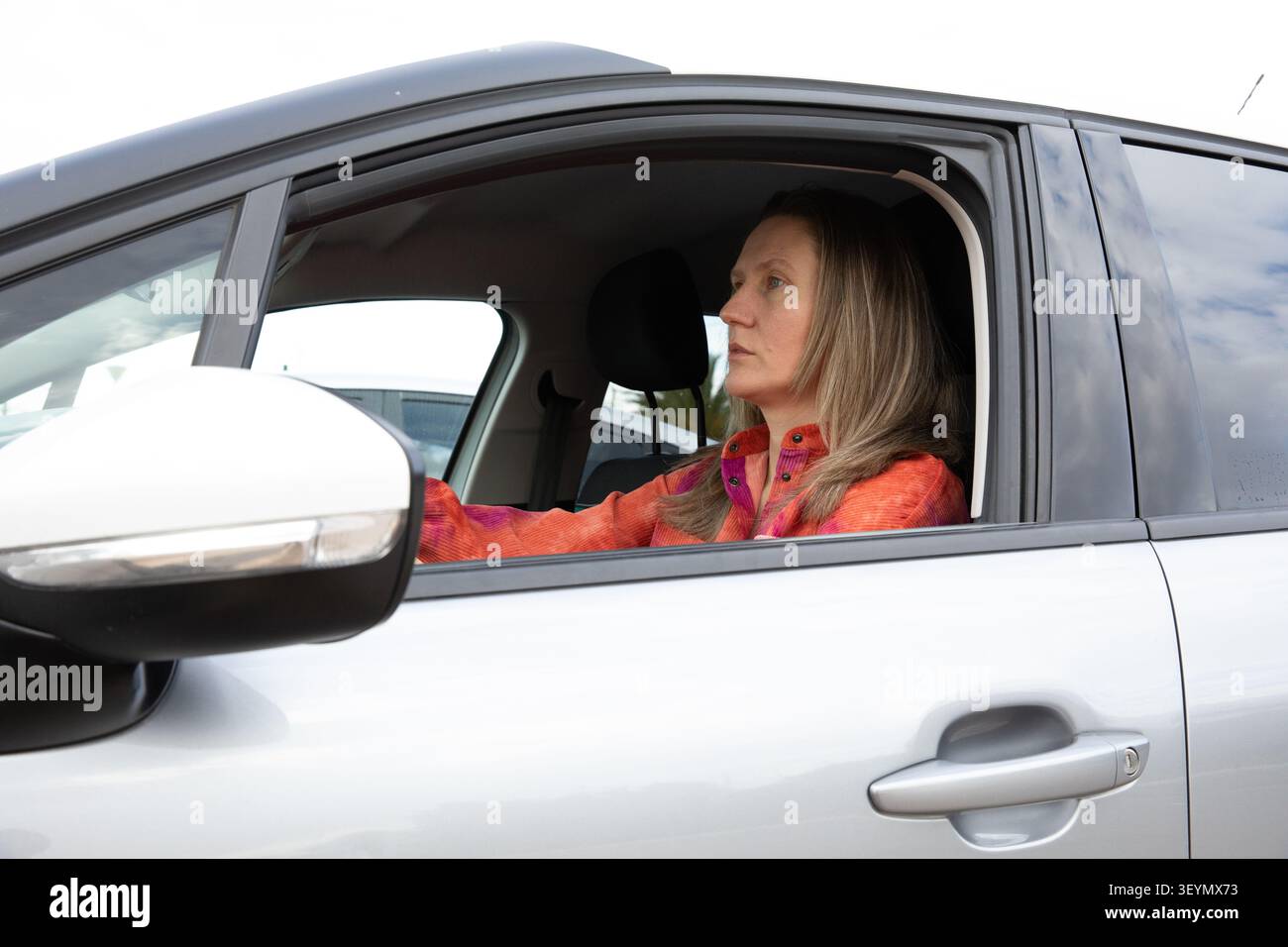 Fahrer sitzt tagsüber im Auto und blickt auf dem Parkplatz nach vorne. Aktivität findet tagsüber statt. Horizontal. Stockfoto