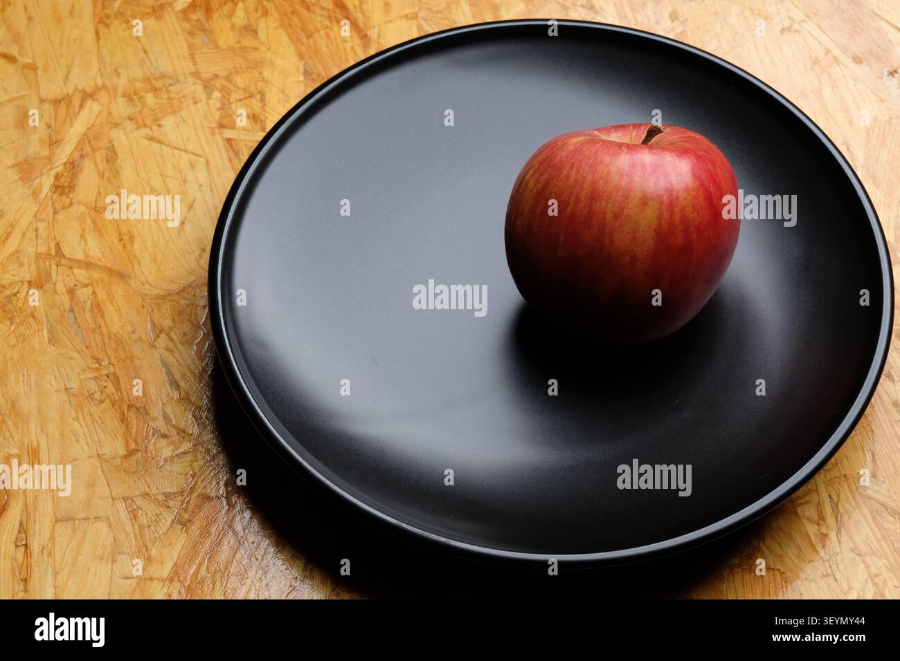 Ein roter Apfel in einer schwarzen Schale auf braunem Holztisch Stockfoto