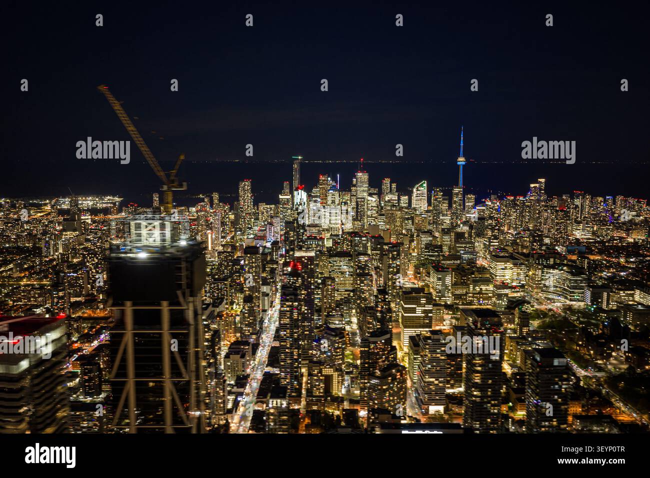 Nächtlicher Blick über die Innenstadt von Toronto mit beleuchteten Hochhäusern, Baukran auf Hochhausvordergrund, dichtem Straßengitter und Stockfoto