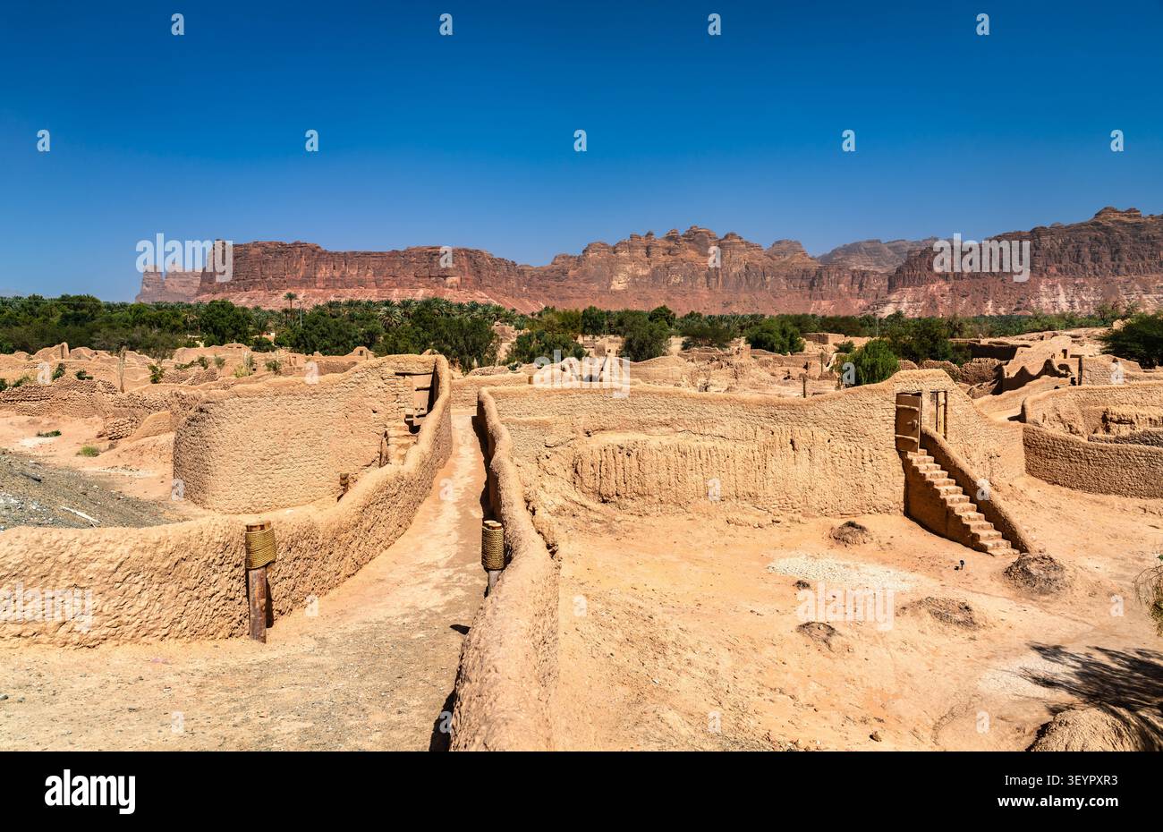 Malerischer Blick auf die historischen Schlammsteinruinen der Altstadt von Alula mit zerklüfteten Sandsteinbergen im Hintergrund in Saudi-Arabien. Stockfoto