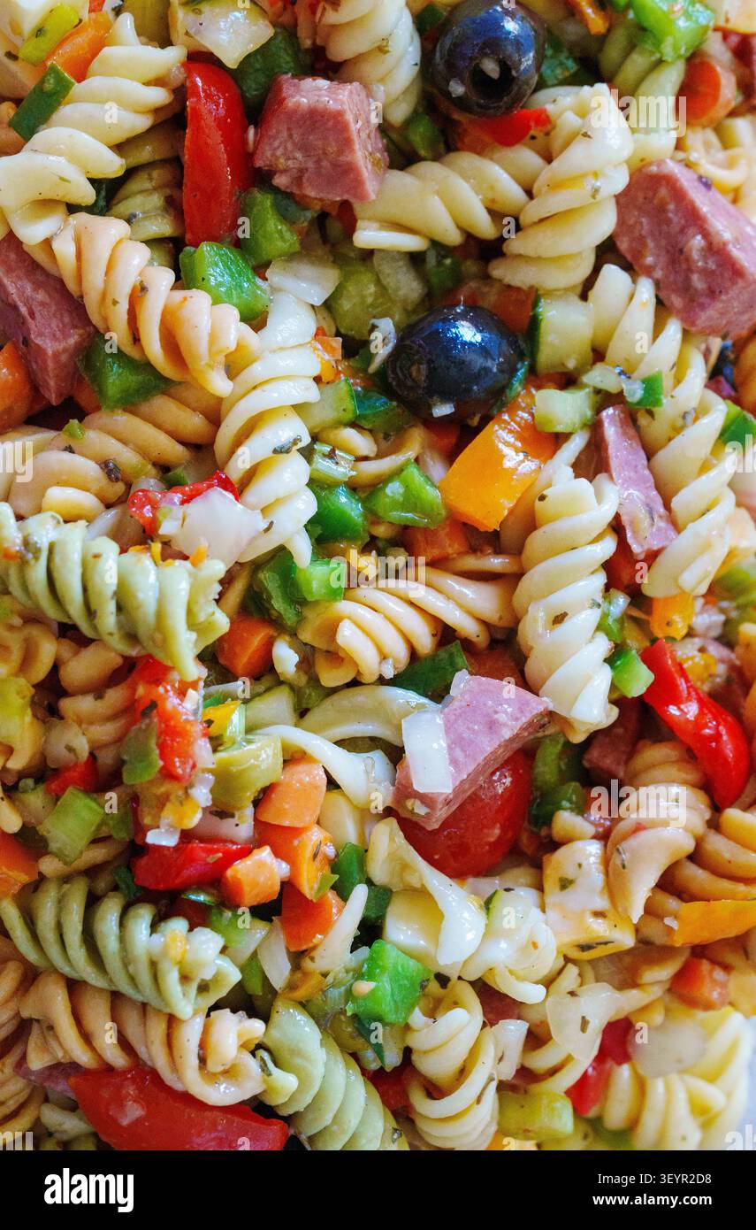 Eine Schüssel enthält Pasta, gemischt mit verschiedenen Gemüse- und Fleischsorten. Der Salat hat verschiedene Formen von Nudeln, Paprika, Oliven und Fleischwürfeln Stockfoto
