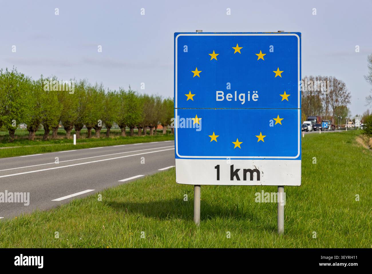 Belgien: Blaues Schild an der Grenze zur Europäischen Union mit gelben Sternen, das die Einfahrt nach Belgien in 1 km, neben einer Landstraße, anzeigt. Stockfoto