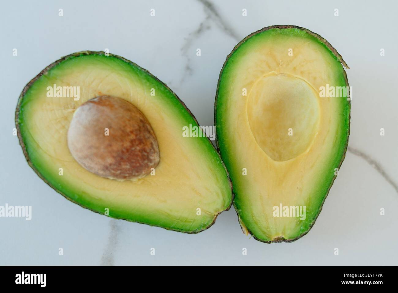 Avocadohälften auf Marmoroberfläche geschnitten frisch und natürlich Top-down Perspektive Saatgut-Fotografie gesund essen grün gelb kommerziell Licht Stockfoto