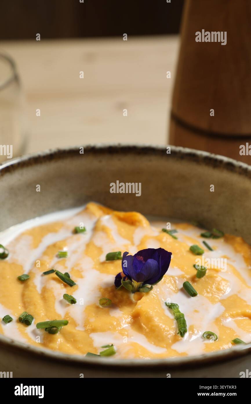 UN bol de purée de légumes se trouve sur une table en bois. La purée EST orange et garnie de Crème, de ciboulette et d'une fleur. UN élément décoratif Stockfoto