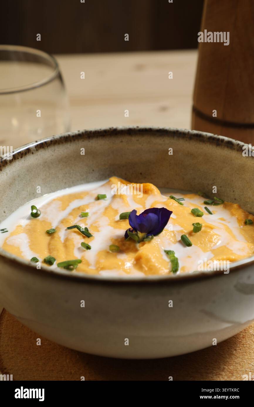 UN bol de Crème épaisse avec de la purée orange et des touches de vert. Des herbes sont ajoutées sur le dessus avec une fleur violette. Le plat EST PR Stockfoto