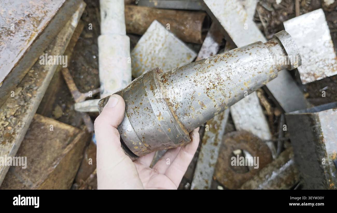 Eine Hand, die einen Werkzeughalter mit rostigem Metallspindel und konischem Schaft über einem Stapel Stahlschrott hält. Stockfoto