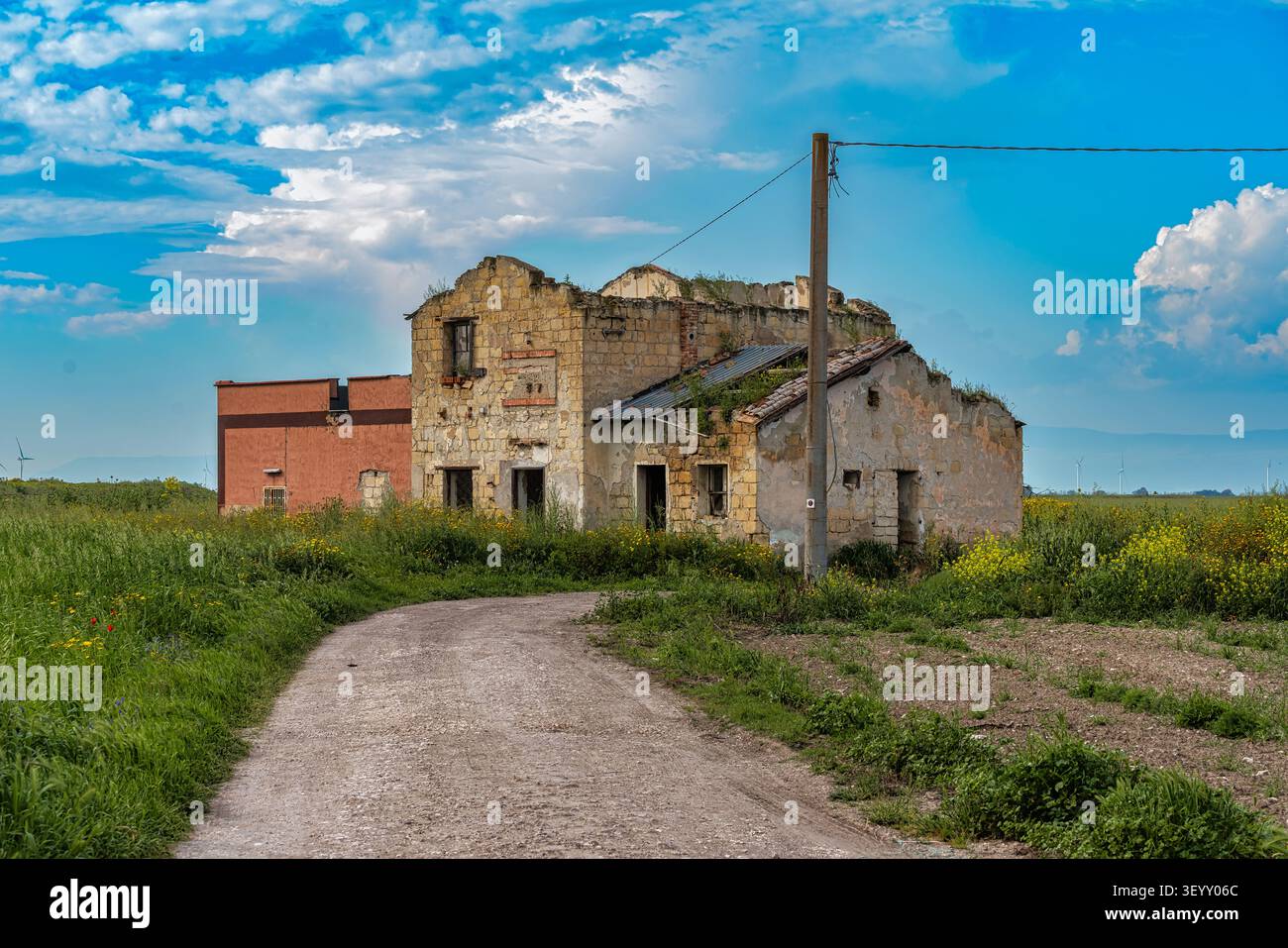 Ein verfallenes, verlassenes Bauernhaus in der Landschaft von Cerignola, mit einem Feldweg, der sich zum baufälligen Gebäude schlängelt. Cerignola, Apulien Stockfoto