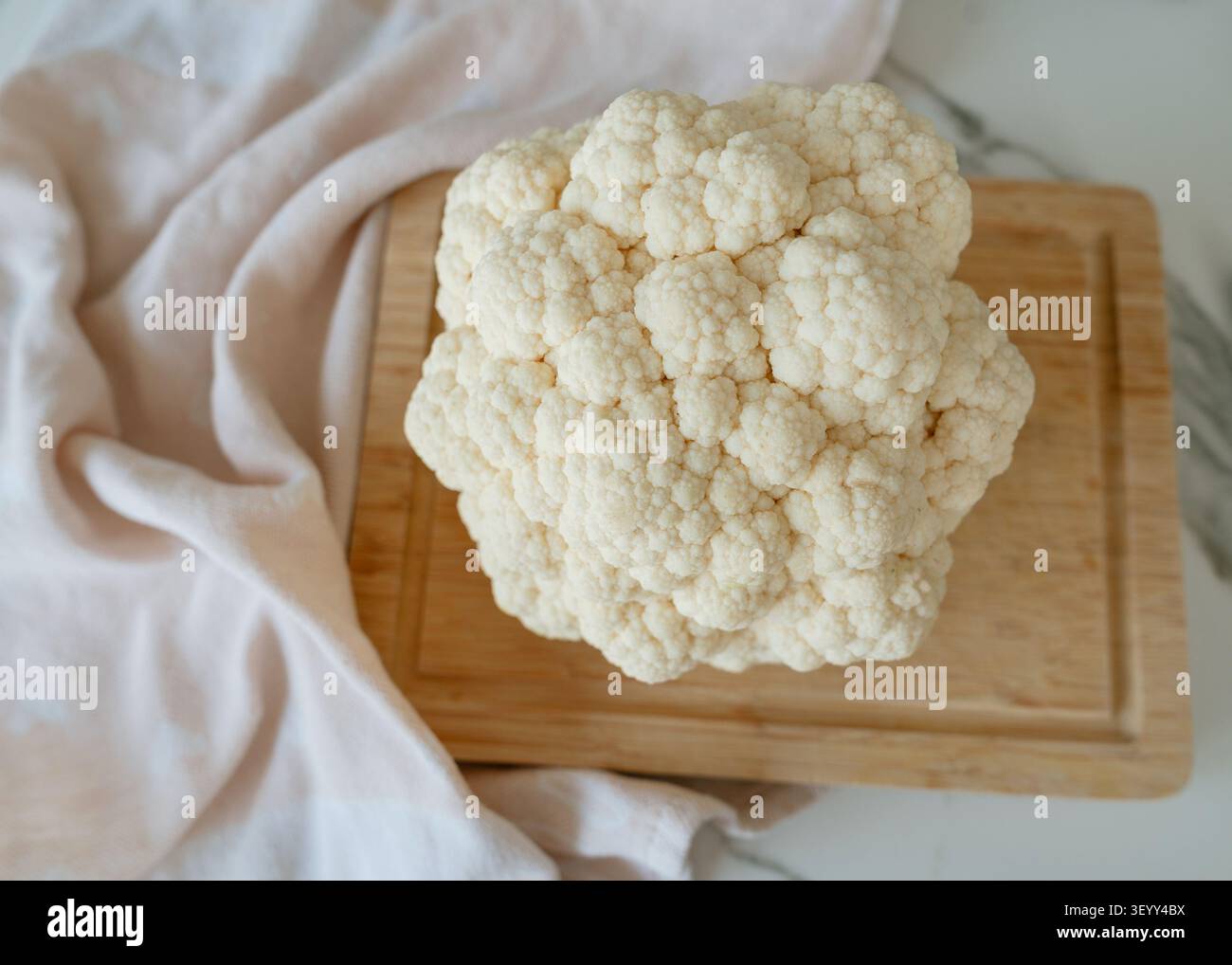 Eine Nahaufnahme von Blumenkohl auf einem hölzernen Schneidebrett in einer sauberen Küchenumgebung, aufgenommen von oben nach unten, die das frische und gesunde unterstreicht Stockfoto