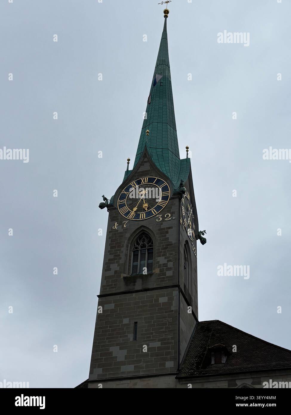 Nahaufnahme der eleganten Uhr und des türkisfarbenen Turms der Fraumünster-Kirche vor einem bewölkten Himmel - Smartphone-aufgenommenes Stockfoto