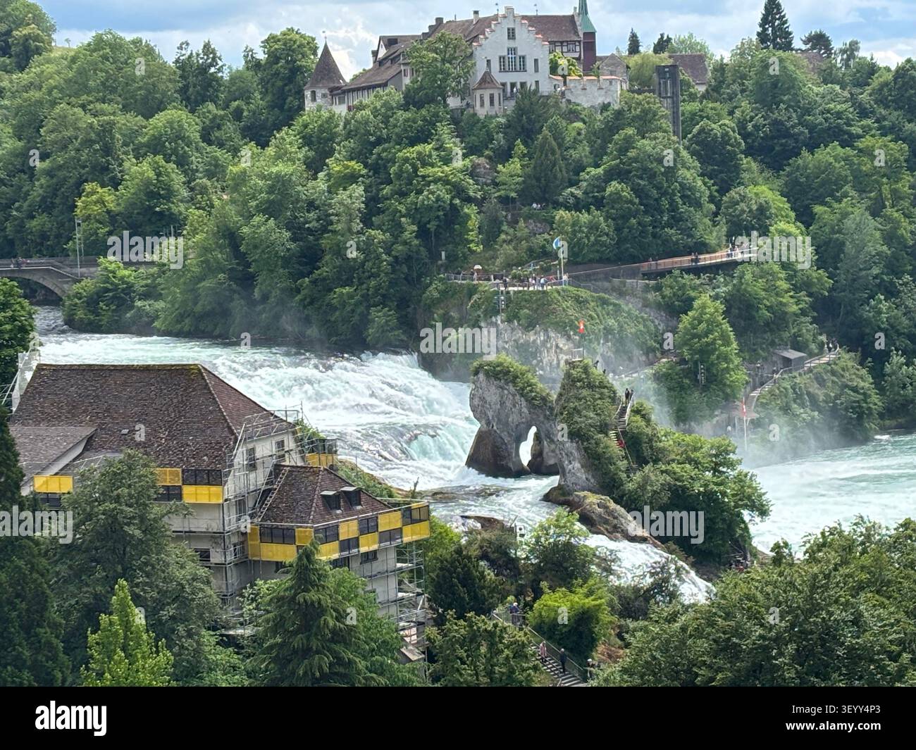 Hohe Blickwinkelansicht der massiven Rheinfälle, die um Felsformationen tosen, mit Schloss Laufen auf dem Hügel Stockfoto