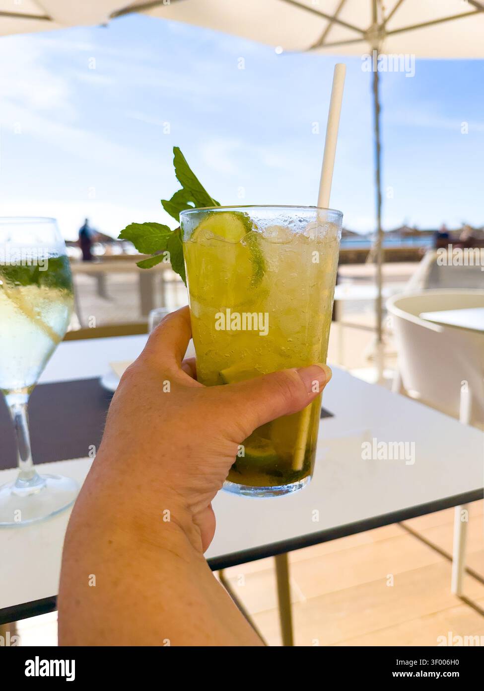 Halten Sie einen kalten Mojito-Cocktail mit Limette und Minze an einem Tisch auf der Terrasse - Smartphone-aufgenommenes Stockfoto
