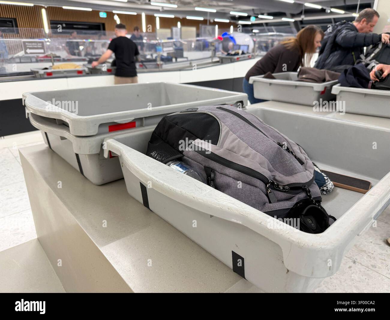 Rucksack & persönliche Gegenstände in grauen Plastikbehältern am Sicherheitskontrollpunkt des Flughafens Newcastle mit Passagieren im Hintergrund Stockfoto