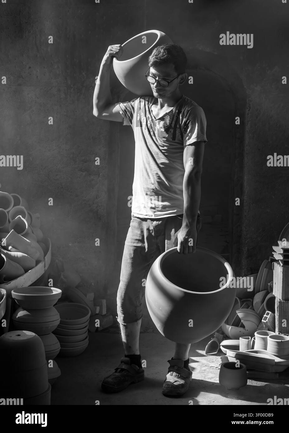 Menemen, Türkei - 10. Juli 2021: Schwarzweiß-Ansicht eines jungen Handwerkers mit handgefertigten Terrakotta-Gläsern in einer traditionellen Werkstatt Stockfoto