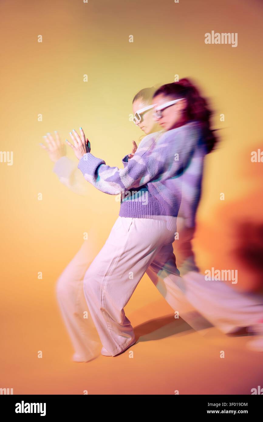 Die junge Tänzerin bewegt sich in einem trippalen Objektiveffekt mit Neonlichtern, wodurch lebendige Bewegungsunschärfen und doppelte Belichtung entstehen. Stilvolle Streetwear, energiegeladene Pos. Stockfoto