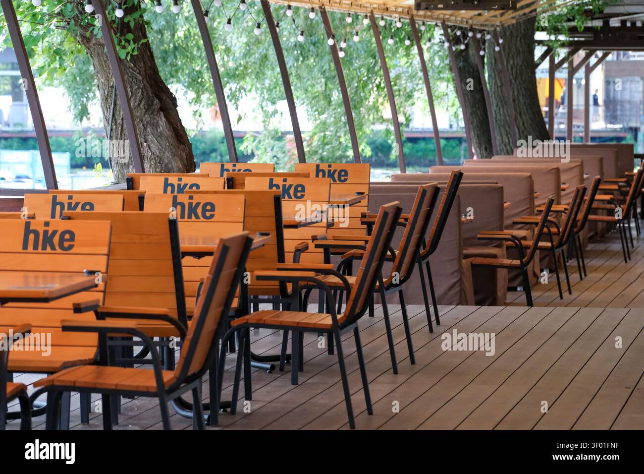 KIEW, UKRAINE, 5. JULI 2026, leere Außenterrasse des Restaurants mit Holztischen und Stühlen, die an einem Sommertag am Fluss für Besucher vorbereitet werden. Stockfoto