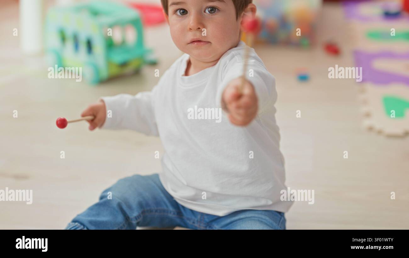 Der Junge sitzt mit Drumsticks und klopft in einem Spielzimmer an ein Spielzeuginstrument, die Hände sind sichtbar und absichtlich, ruhige Konzentration. Stockfoto