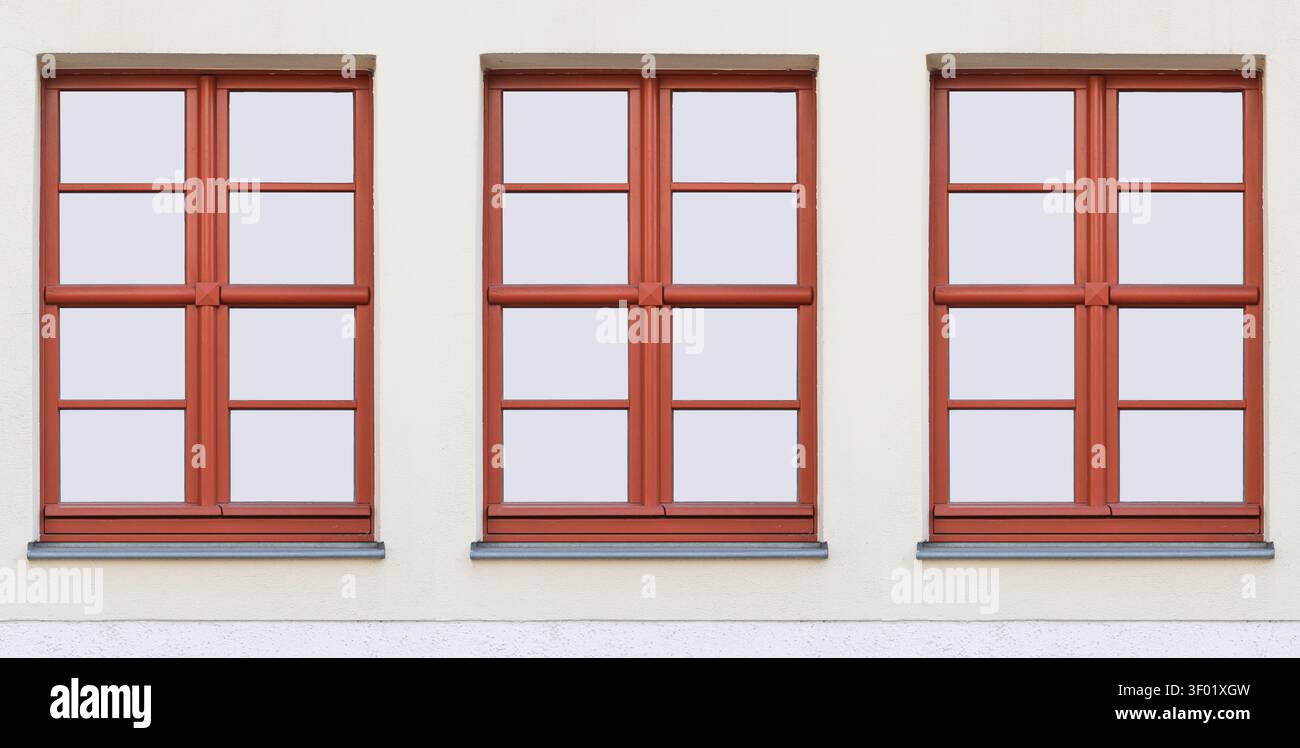 Drei braune Holzfenster, die an einer weißen Gebäudefassade angeordnet sind. Architekturhintergrund für Heimrenovierung, Konstruktionsdesign und Wohneigentum Stockfoto