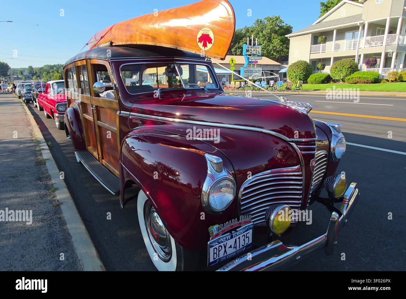 Ein uralter kastanienbrauner Kombi mit Holzkanu auf dem Dach, der bei einem Oldtimer-Event auf einer Straße geparkt wurde. Stockfoto