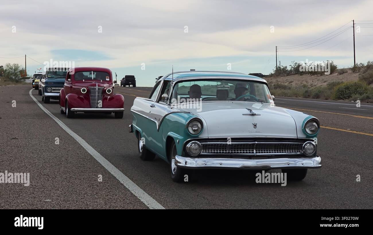 Eine klassische, türkisfarbene und weiße Limousine, die auf einer Autobahn fährt, gefolgt von anderen Oldtimern in einer Gruppe. Stockfoto