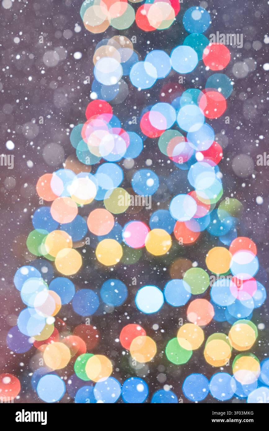 Abstrakter vertikaler Weihnachtshintergrund mit kühl gefärbten Bokeh-Lichtern, die die Umrisse eines Weihnachtsbaums auf einem lila Hintergrund bilden. Fallende Schneeflocken Stockfoto