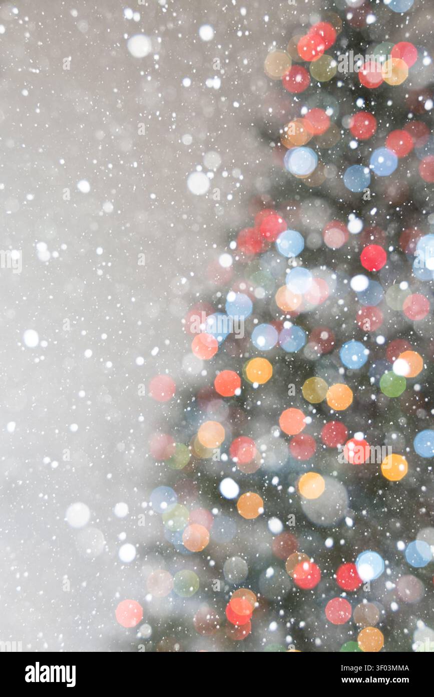Vertikaler Weihnachtshintergrund mit weichen warmen Bokeh-Lichtern und der zarten Umrisse eines Weihnachtsbaums auf einem hellbeigen Hintergrund. Fallender Schnee Stockfoto