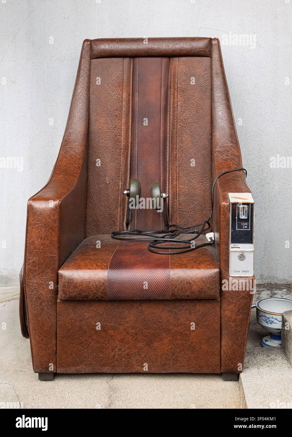 Vintage brauner, münzbetriebener Massagesessel aus Leder, der drinnen vor einer einfachen Hintergrundwand steht, Kyoto, Japan Stockfoto