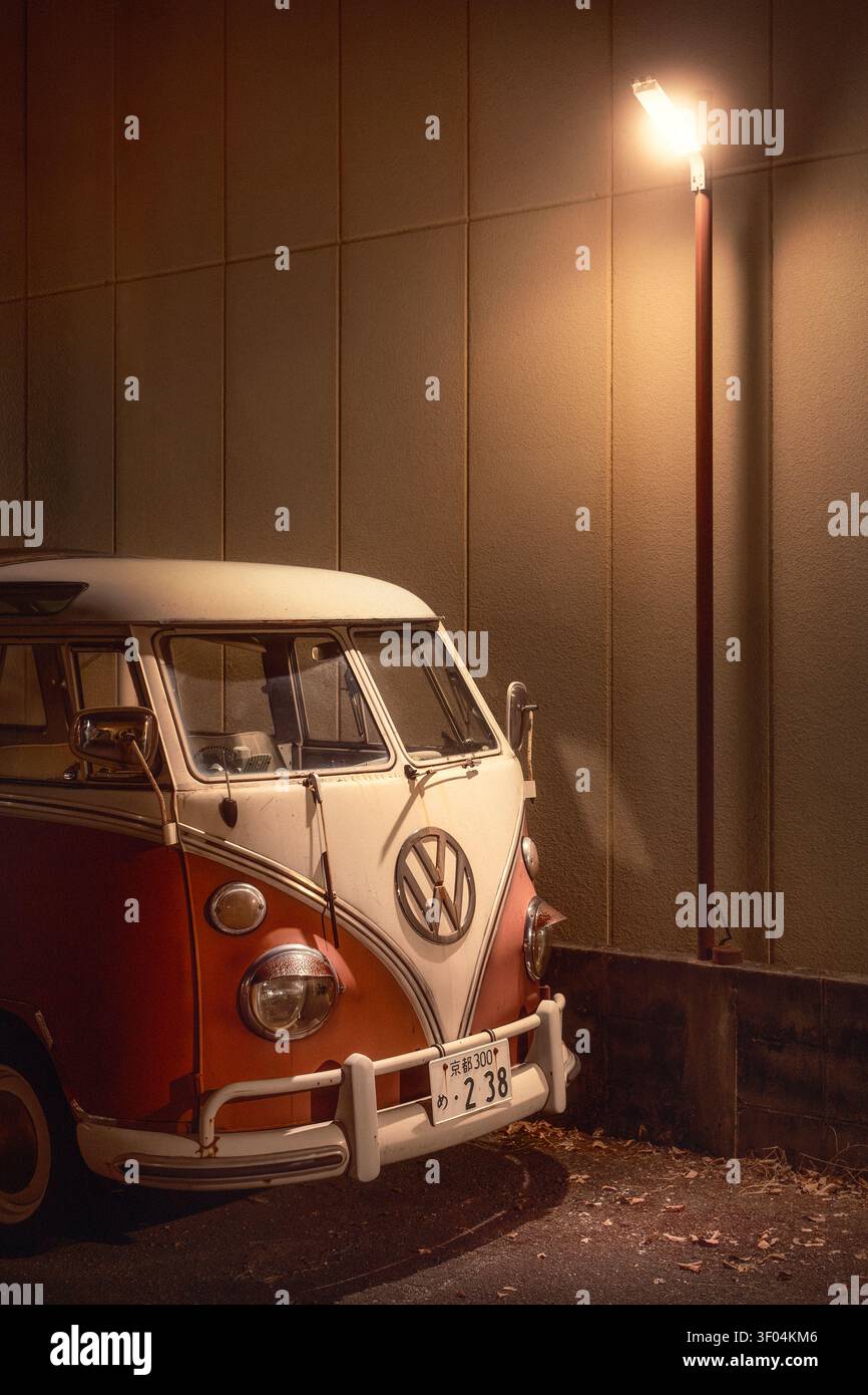 In einer ruhigen Seitenstraße in Kyoto, Japan, steht ein Vintage-Van des Typs Volkswagen T1, dessen rot-weißes Gehäuse das warme Leuchten einer Straßenlaterne einfängt. Stockfoto