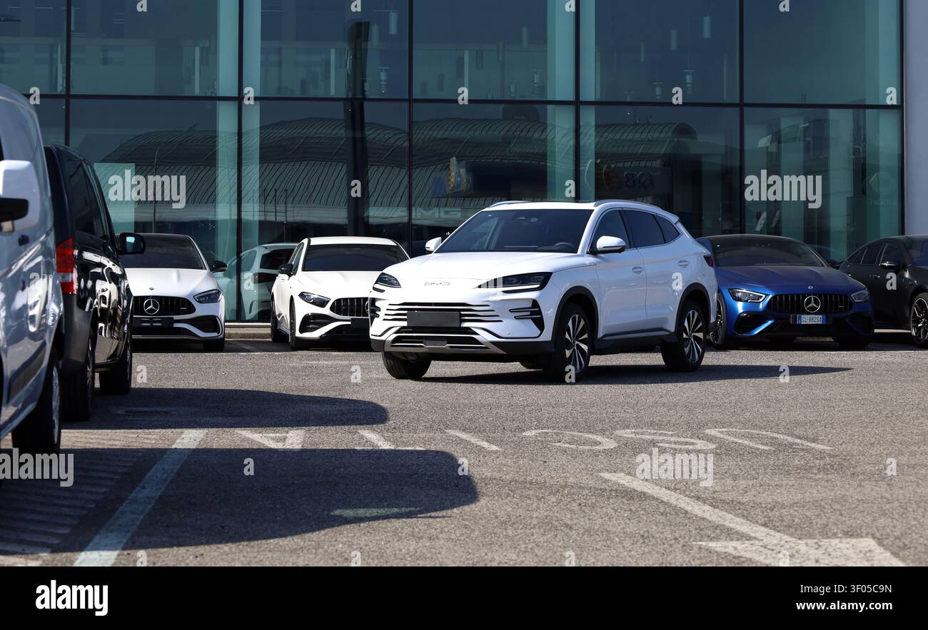 Udine, Italien. 9. März 2025. Weißer BYD Song Plus in der Ausstellung des offiziellen Händlers. Glasfassade und Mercedes-Benz-Autos im Hintergrund Stockfoto