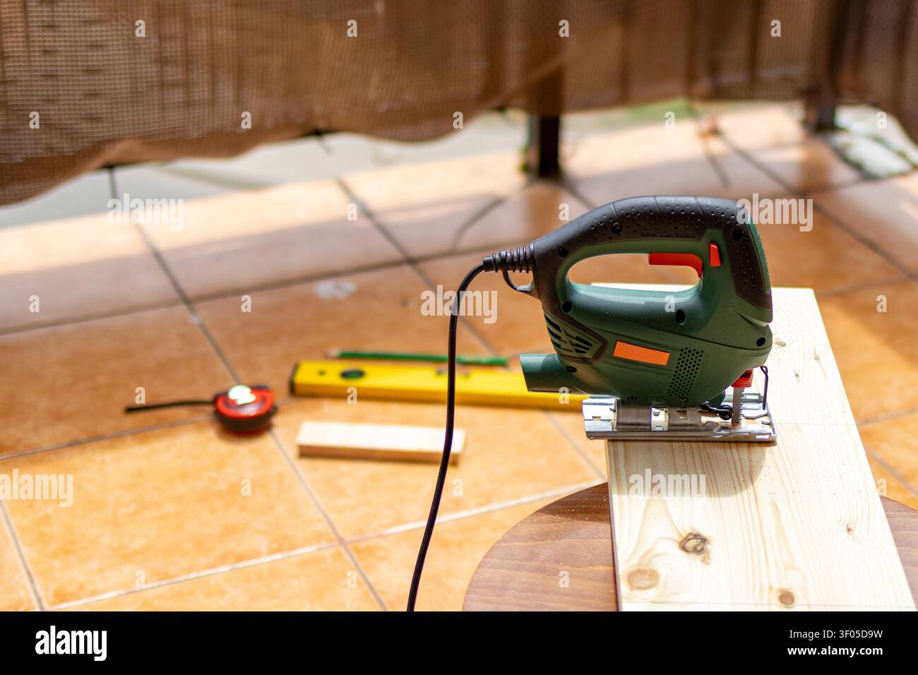 Elektrische Stichsäge, Nivellierband und Maßband ruhen auf Holzbrettern, bevor das Schneiden während eines DIY-Möbelprojekts beginnt. Präparationskonzept, Holzarbeiten Stockfoto