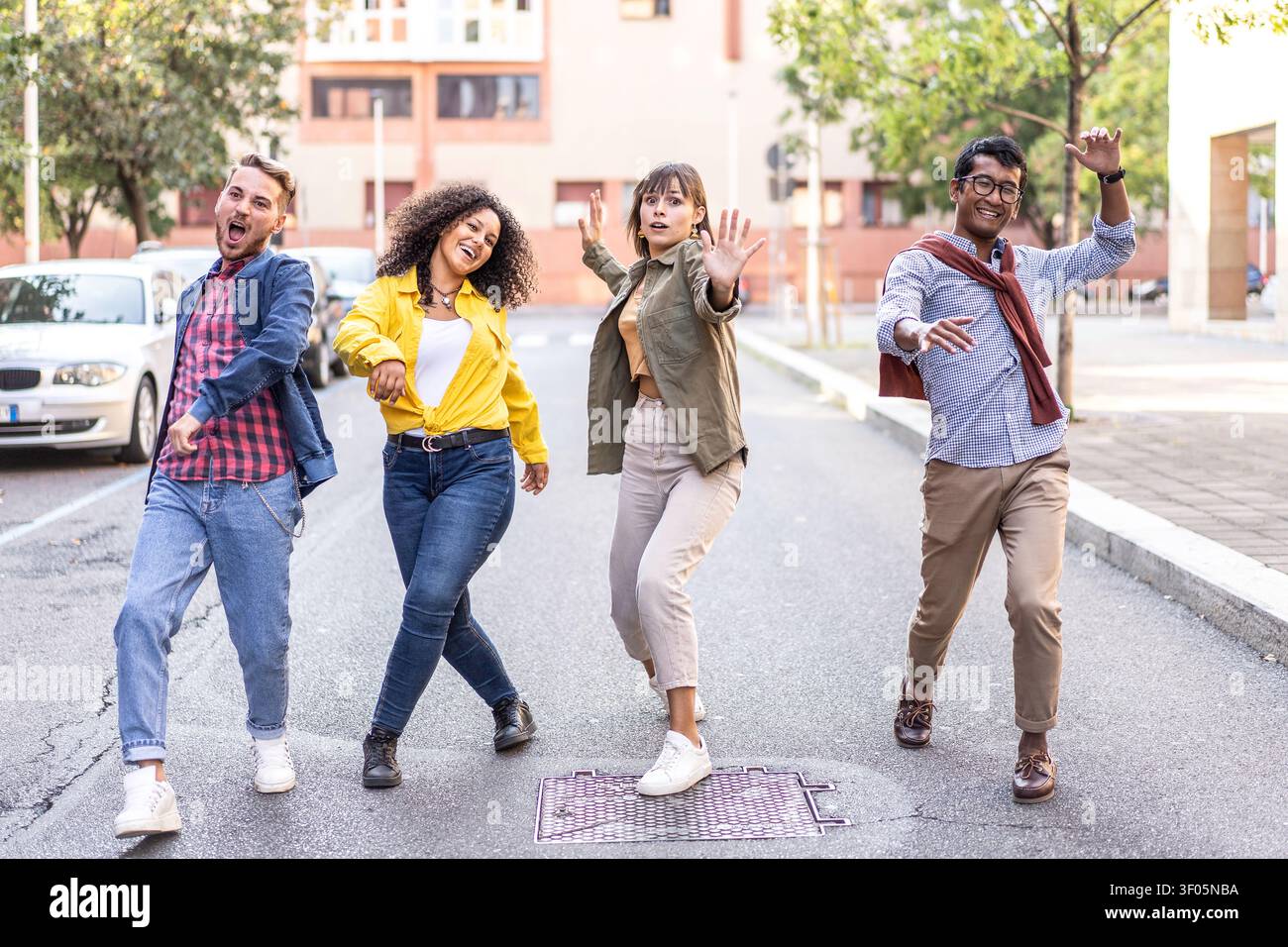 Energetische, vielfältige Freunde tanzen verspielt auf einer ruhigen Stadtstraße. Multiethnische Millennials und Gen Z zeigen unbeschwerte Freude und Bewegung im Freien. Urban y Stockfoto