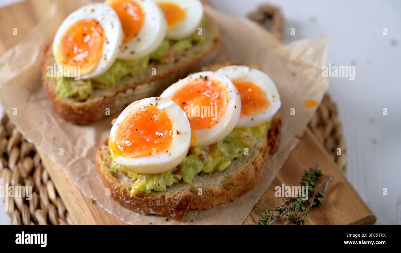 Zwei Scheiben knuspriger Sauerteig mit cremigem Avocado-Brei und marmelierten weichen gekochten Eiern. Die Szene bietet helles natürliches Licht und rustikale Textur Stockfoto