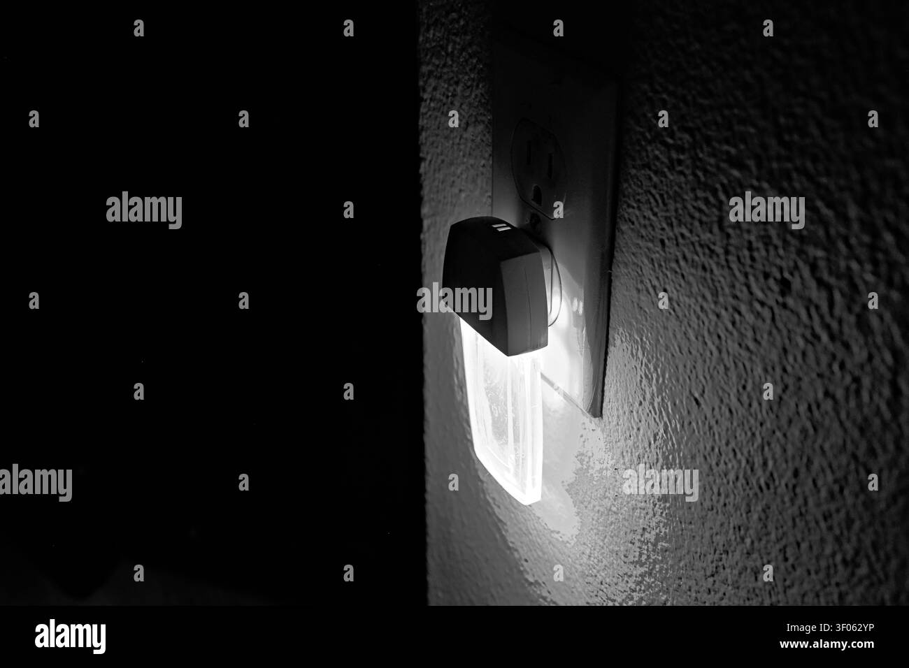Schwarz-weißes Nachtlicht, das in eine Steckdose eingesteckt ist, zeigt sanfte Beleuchtung, Textur und Heimnightsicherheit. Stockfoto